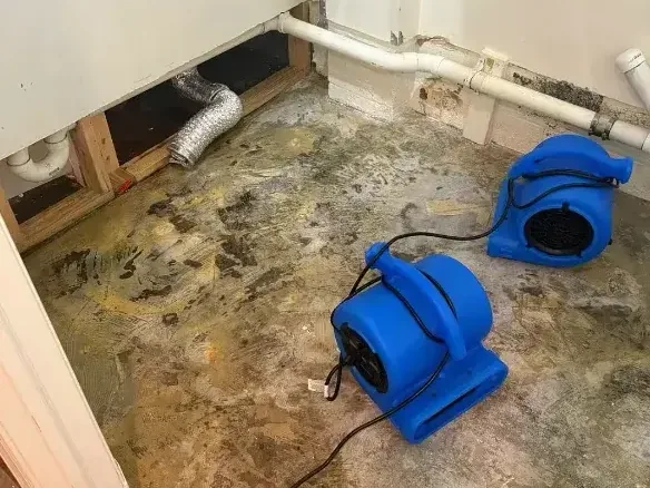 Air movers aimed at a bare subfloor after a pipe leak